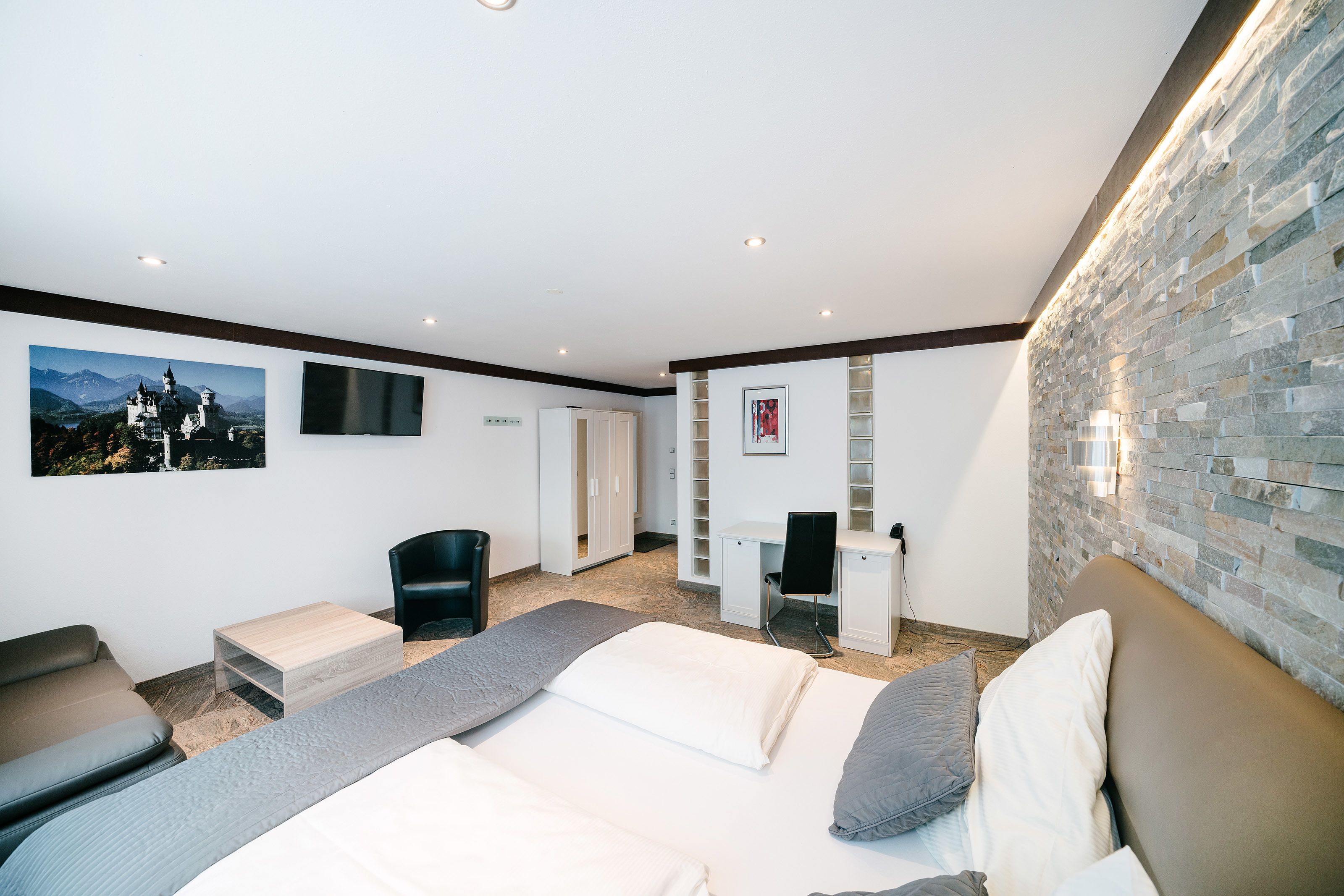 A modern hotel room with a large bed, a desk, and a wardrobe.