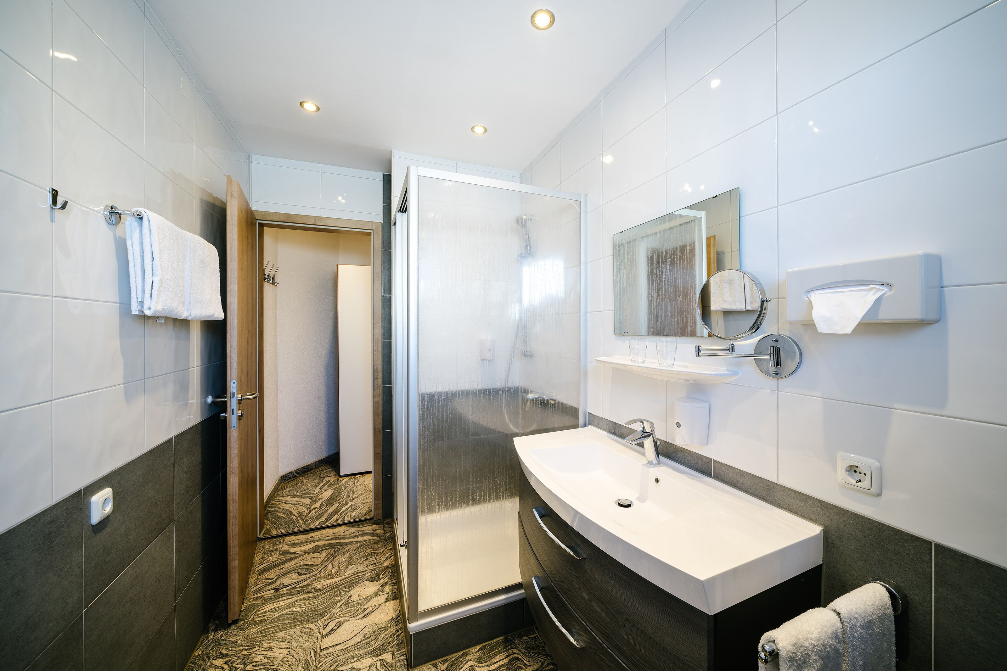 A modern bathroom with a glass shower enclosure, a white sink, and a mirror above it.