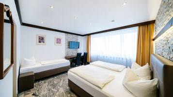 Ein Hotelzimmer mit einem großen Bett, einem kleineren Bett, einem Schreibtisch mit Stühlen, einem Fernseher und einer Wand mit Steinverkleidung.