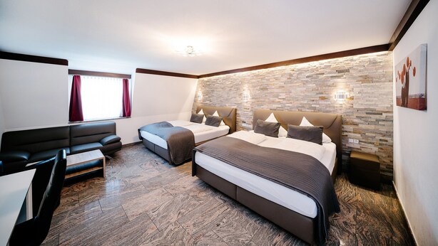 Una habitación de hotel moderna con dos camas, un sofá, suelo de madera y pared de piedra.