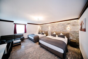 A modern hotel room with two beds, a sofa, a wooden floor, and a stone wall. - Central City Hotel (Fuessen)