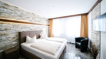 Una habitación de hotel moderna con pared de ladrillo, una cama grande con ropa blanca, un sillón de cuero negro y un televisor de pantalla plana en la pared.