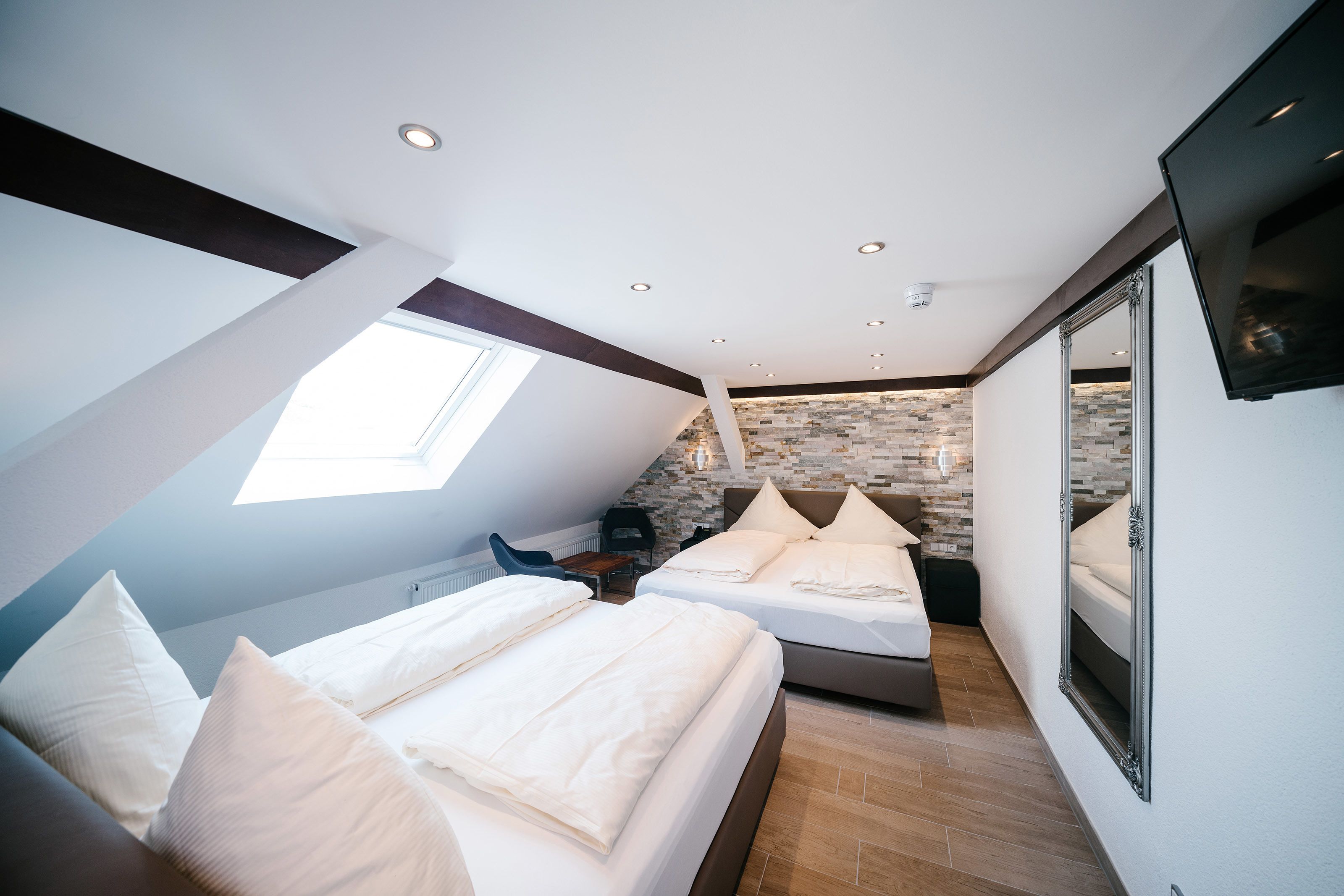 A modern bedroom with a skylight, a stone wall, and a large mirror.
