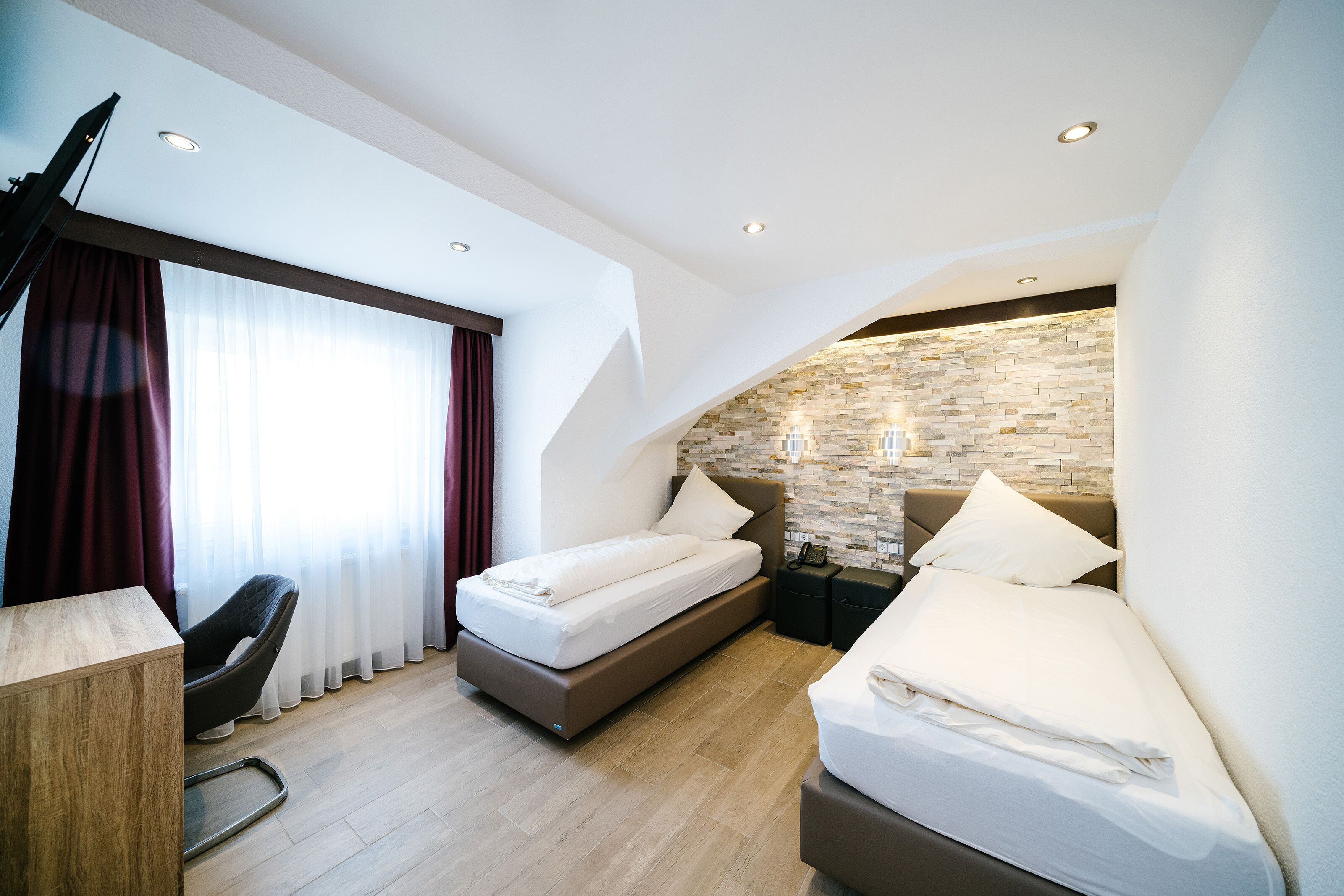 A modern hotel room with a bed, a desk, a chair, and a stone accent wall.