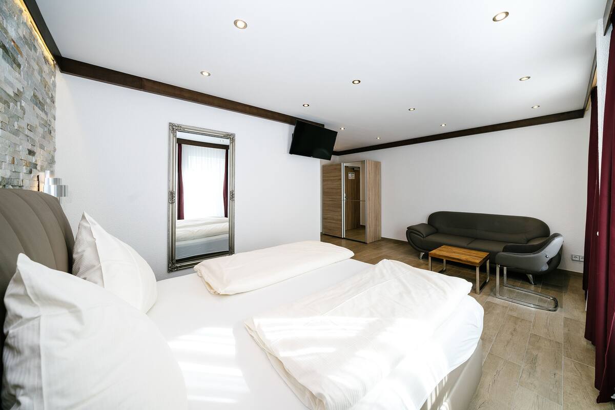 A hotel room with a bed, a sofa, a wooden cabinet, and a television mounted on the wall.
