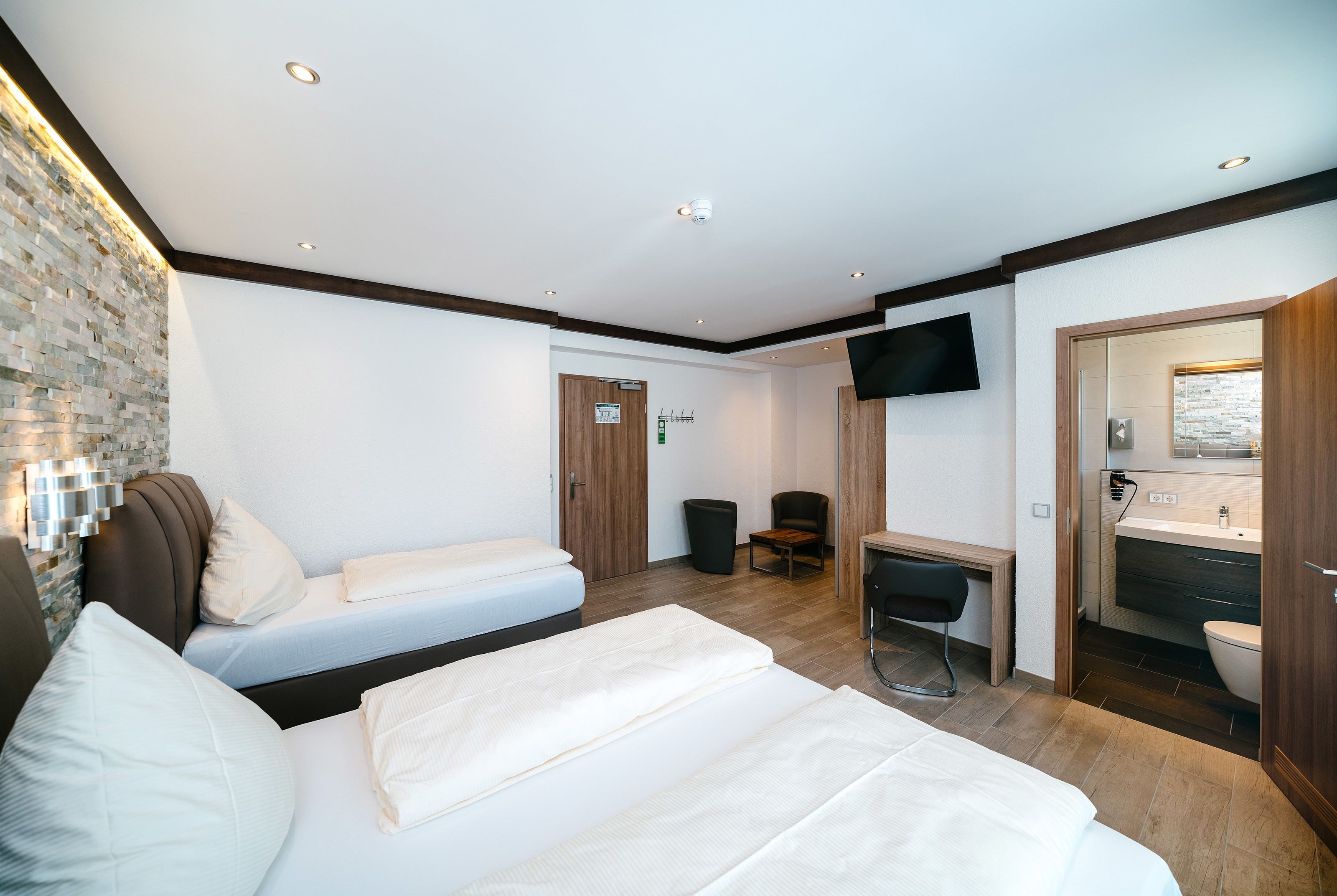 Ein Hotelzimmer mit zwei Betten, einem Schreibtisch, einem Sessel, einem Fernseher und einem Badezimmer.