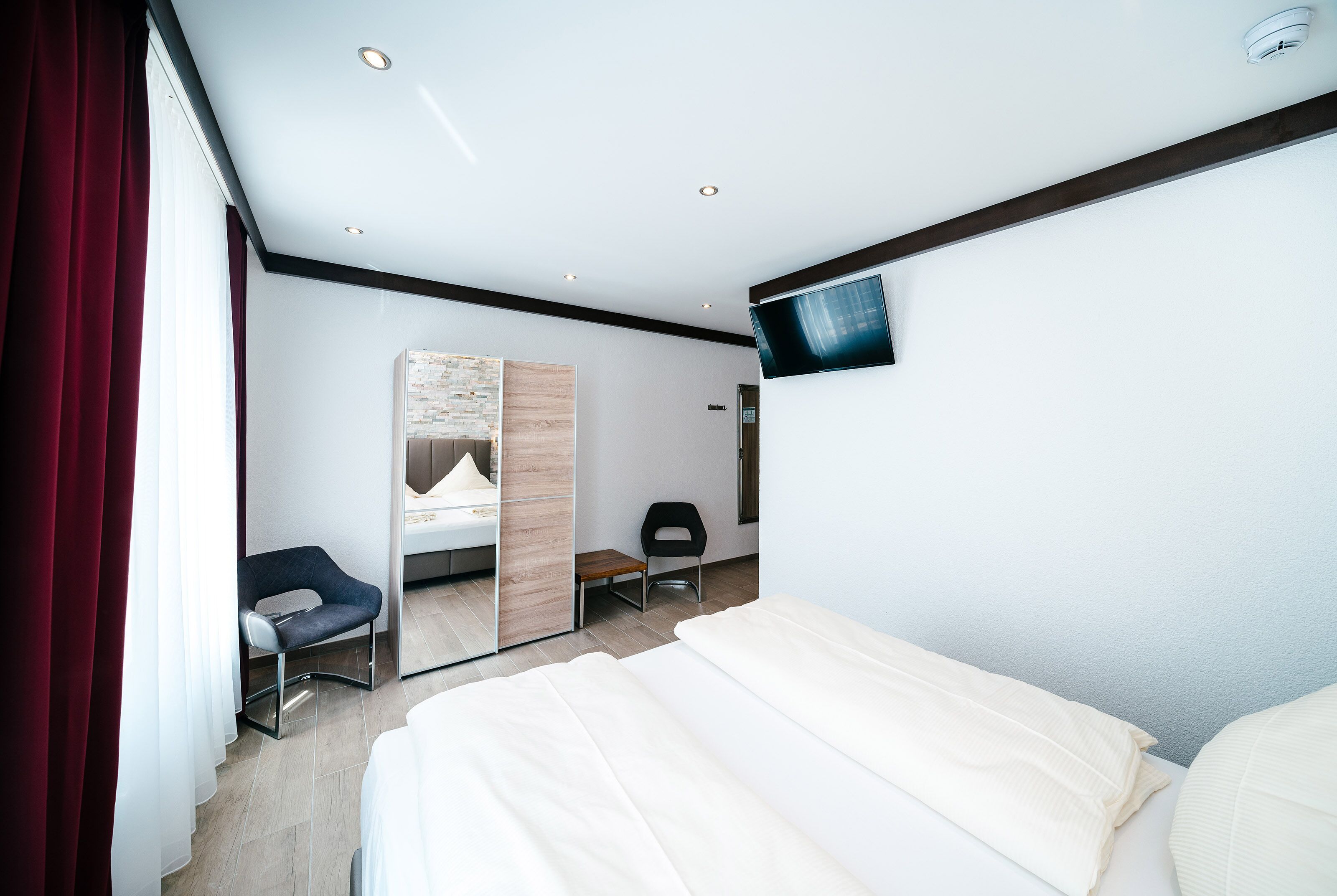 Quarto de hotel moderno com cama, escrivaninha, cadeira, televisão e espelho.