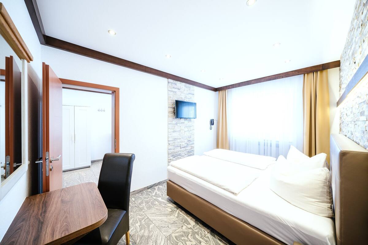 A hotel room with a bed, a TV mounted on the wall, a wooden table, and a chair.
