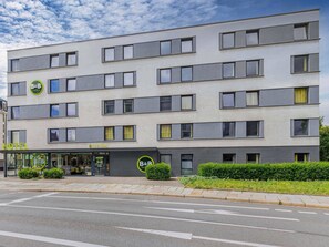 A modern hotel building with a reception area, multiple floors, and a clear sky. - B&B HOTEL Dresden-Messe (Dresden)