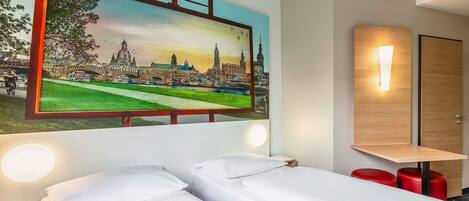 A hotel room with a bed, a nightstand, a wall-mounted light, and a painting of a cityscape.