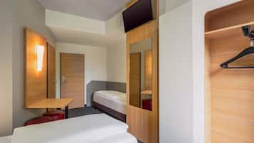 A modern hotel room with a bed, a desk, a mirror, and a TV mounted on the wall.