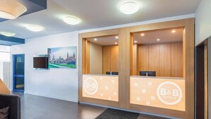 Un hall d’accueil d’hôtel avec deux comptoirs de réception, une peinture représentant un paysage urbain au mur et un aménagement intérieur moderne.