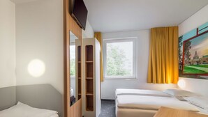 Une chambre d’hôtel avec deux lits simples, une armoire en bois, un bureau, une fenêtre avec des rideaux et un tableau au mur.