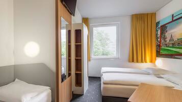 Ein Hotelzimmer mit zwei Einzelbetten, einem Holzschrank, einem Schreibtisch, einem Fenster mit Vorhängen und einem Bild an der Wand.