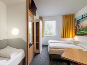 A hotel room with two single beds, a wooden wardrobe, a desk, a window with curtains, and a painting on the wall. - B&B HOTEL Dresden-Messe (Dresden)