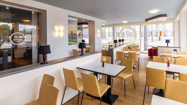 A modern hotel lobby with a reception desk, seating area, and large windows offering views of the city. - B&B HOTEL Dresden-Messe (Dresden)