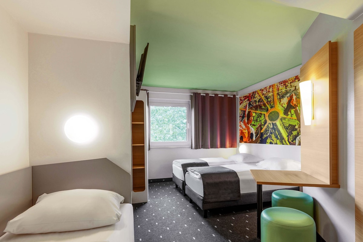 A hotel room with a bed, two bedside tables, a desk, a chair, and a window with curtains.