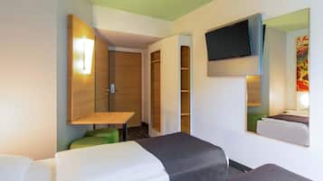 Habitació d'hotel amb dos llits, televisió penjada a la paret, armari de fusta i una taula petita amb una cadira verda.