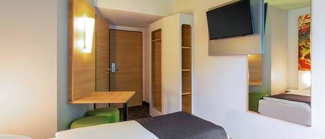 A hotel room with two beds, a TV mounted on the wall, a wooden wardrobe, and a small table with a green chair.