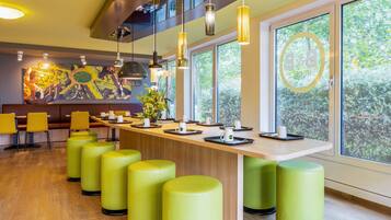 A modern restaurant with a long counter, yellow chairs, and green stools.