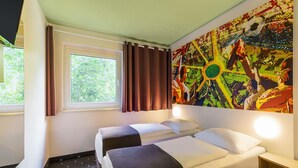 A hotel room with two beds, a window with curtains, a colorful abstract painting on the wall, and a small wooden table. - B&B Hotel Dortmund-Messe (Dortmund)