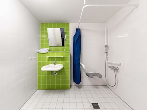 A small bathroom with a white sink, a mirror, a green wall, and a shower. - B&B Hotel Dortmund-Messe (Dortmund)
