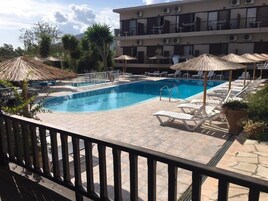 A pool area with lounge chairs and umbrellas, surrounded by a building with multiple balconies.