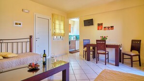 Habitación de hotel con cama, una pequeña mesa de comedor con sillas, televisor montado en la pared y un balcón visible a través de una puerta abierta.