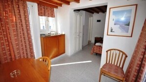 Una habitación compacta con una mesa de comedor de madera, una pequeña zona de cocina y una única silla de madera.