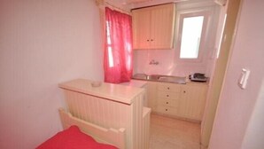 Una habitación pequeña y funcional con cama, kitchenette y ventana con cortina.