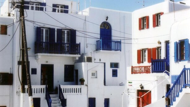 Un edificio blanco con balcones azules y contraventanas rojas, que presenta una escalera que conduce a la entrada.