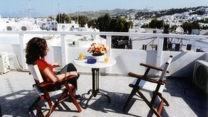 Terraza con dos sillas y una mesa, con vistas a un pueblo costero de edificios blancos y barcos.