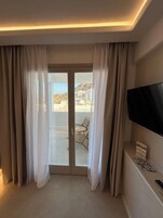 Habitación de hotel con puerta de vidrio corrediza que da a un balcón, un televisor de pantalla plana en la pared y una pequeña mesa con un control remoto.