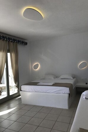 A modern bedroom with a large bed, a bedside table, and a built-in circular light fixture on the ceiling. - Paolas Beach (Mykonos)