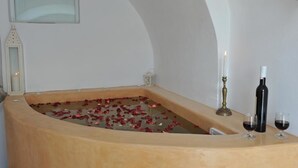 Una bañera llena de pétalos de rosa, una vela y dos copas de vino.