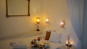 Una habitación de hotel con una cama, una mesita de noche con lámpara, una bandeja con artículos de desayuno y un aplique de pared.