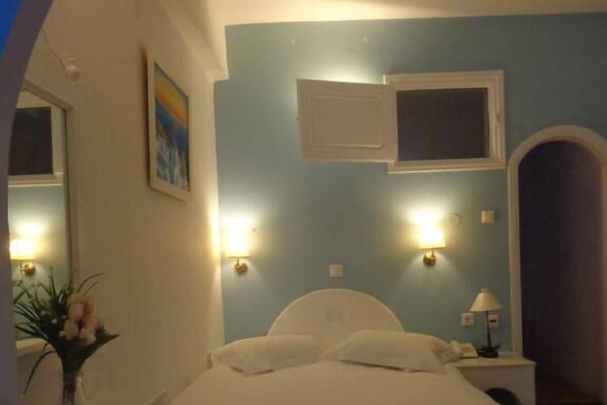 Un dormitorio con cama, una silla, una mesita de noche, una lámpara y un televisor montado en la pared.