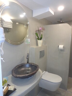 A bathroom with a round mirror, a sink, a toilet, and a shower. - Langas Villas (Santorini)