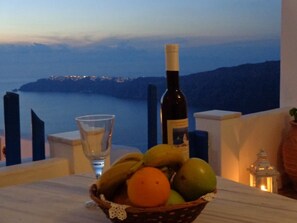 A table with a bottle of wine, a glass, and a basket of fruit. - Langas Villas (Santorini)