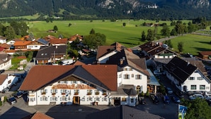 A traditional European village with a central building featuring a courtyard, surrounded by residential houses and a mountainous backdrop. - Hotel Weinbauer (Schwangau)