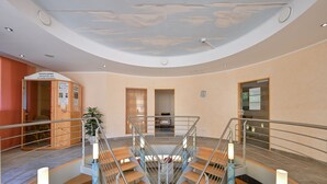 A modern hotel interior with a central spiral staircase, a ceiling mural, and a reception area with a wooden cabinet and informational posters. - Hotel Weinbauer (Schwangau)