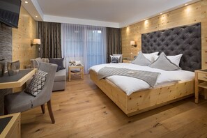 A modern hotel room with a wooden headboard, a large bed with multiple pillows, a wooden desk with a chair, and a small bedside table with a lamp. - Hotel Weinbauer (Schwangau)