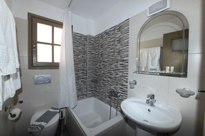 A bathroom with a bathtub, toilet, sink, and a mirror. - Enjoy Villas (Santorini)