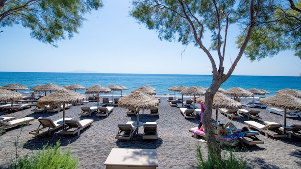 Une plage bordée de rangées de chaises longues et d’ombrelles en chaume, un ciel bleu azur et la mer en toile de fond.