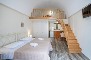 A bedroom with a large bed, a wooden staircase, and a small kitchen area.