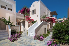 A white building with a stone-paved courtyard, pink bougainvillea, and a staircase. - Enjoy Villas (Santorini)