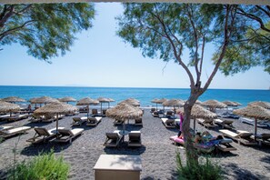A beach with rows of sun loungers and thatched umbrellas, a clear blue sky, and the sea in the background.
