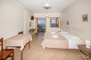 A bedroom with a bed, a desk, and a chair. There is a view of the sea through the window. - Enjoy Villas (Santorini)