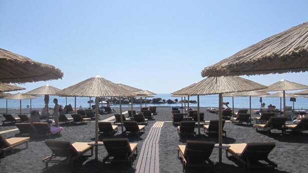 A beachside lounge area with sun loungers and thatched umbrellas, overlooking the sea. - Villa Gambas (Santorini)
