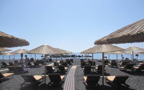 A beachside lounge area with sun loungers and thatched umbrellas, overlooking the sea. - Villa Gambas (Santorini)